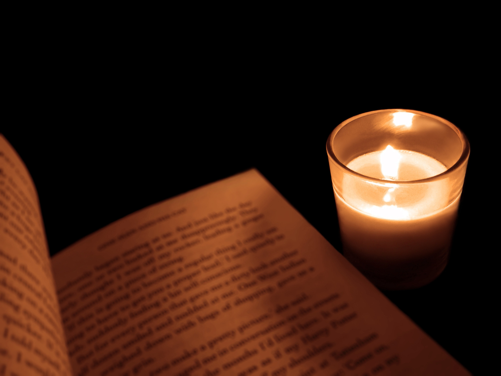 candle in glass holder beside a book