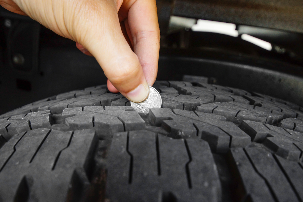A close-up of a hand testing tire tread depth using a coin