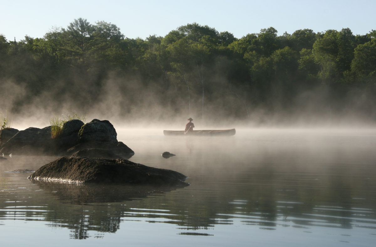A person canoeing on a Misty Lake in the Haliburton Highlands.