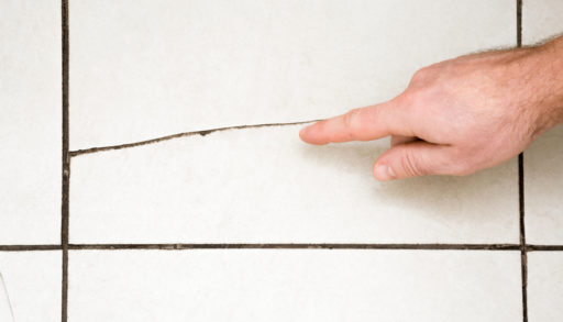 Man's hand finger pointing to the cracked tile on the floor. Building problems and solutions concept.