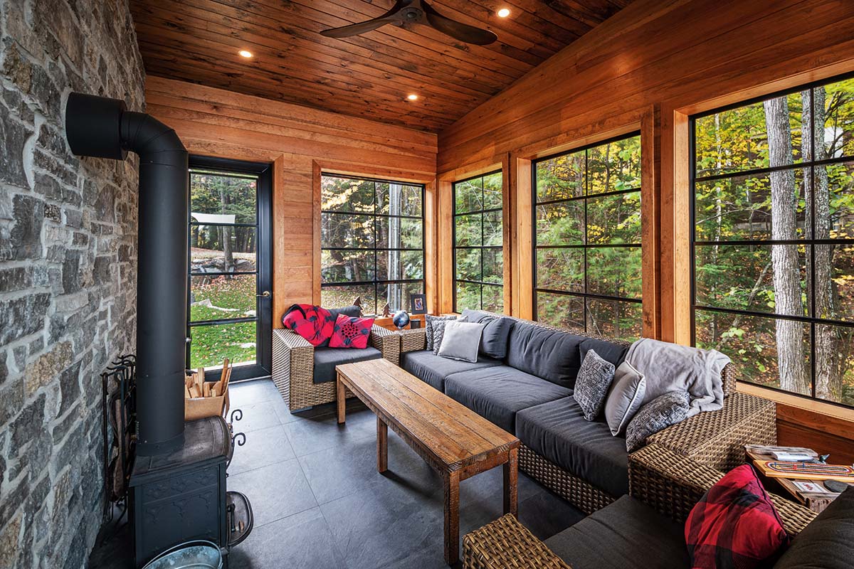 a cottage sunroom with floor to celing windows looking out onto a wooded area