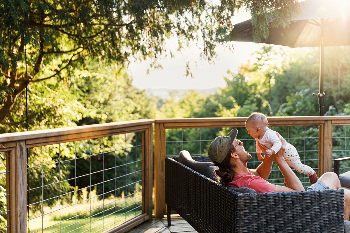 young man holding a baby while the sun sets in the background of a deck