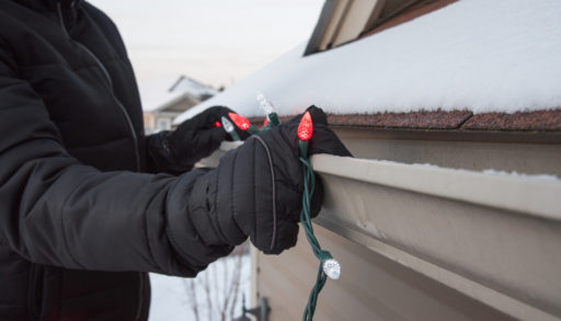 Close-up of a man hanging exterior holiday lights from the roof