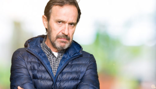 A grumpy man standing outdoors with arms crossed