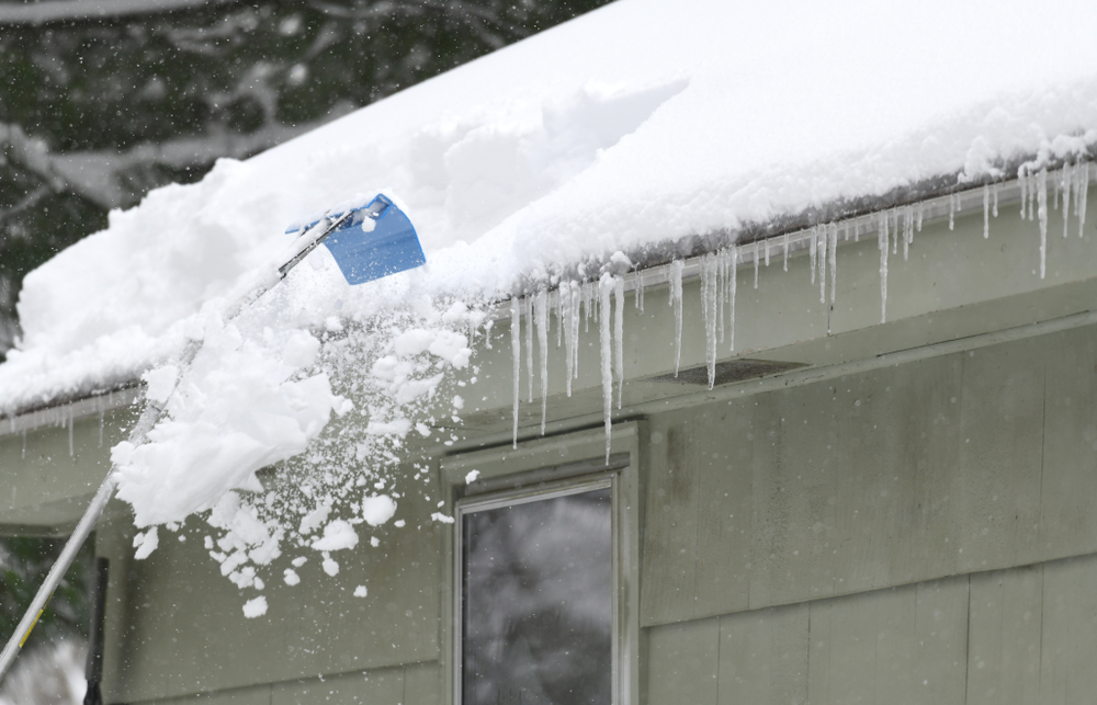 A snow rake removing snow from the roof of a house