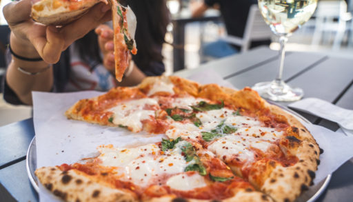 people enjoying fresh pizza on the deck with a glass of white wine