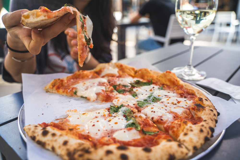 people enjoying fresh pizza on the deck with a glass of white wine