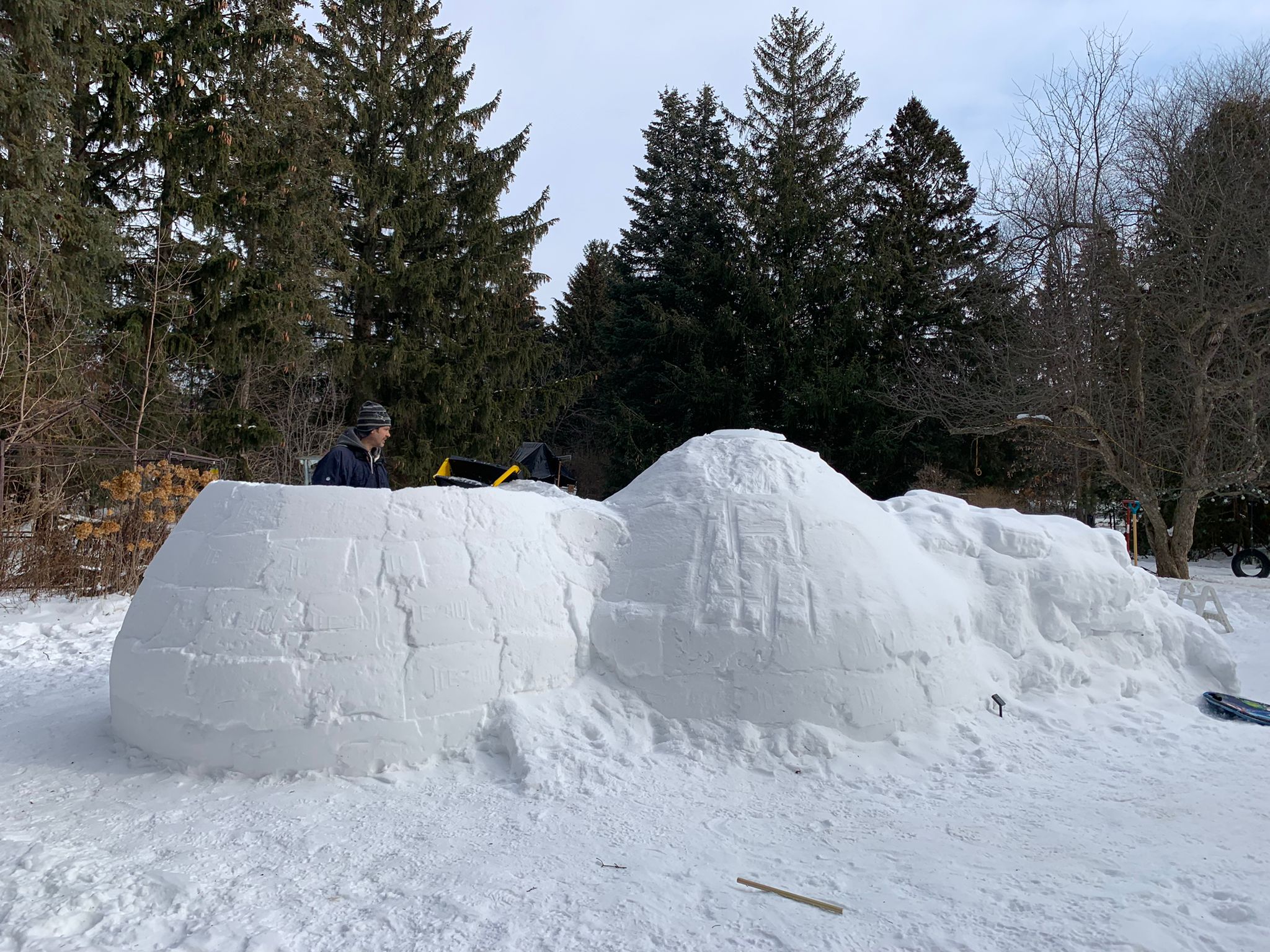 A man standing in the inside of an igloo as he finishes constructing it.