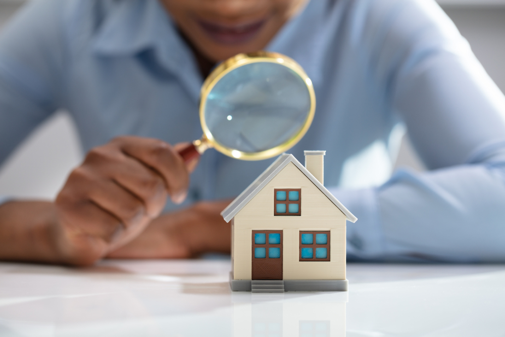 Close up of a woman's hand holding a magnifying glass over a model home