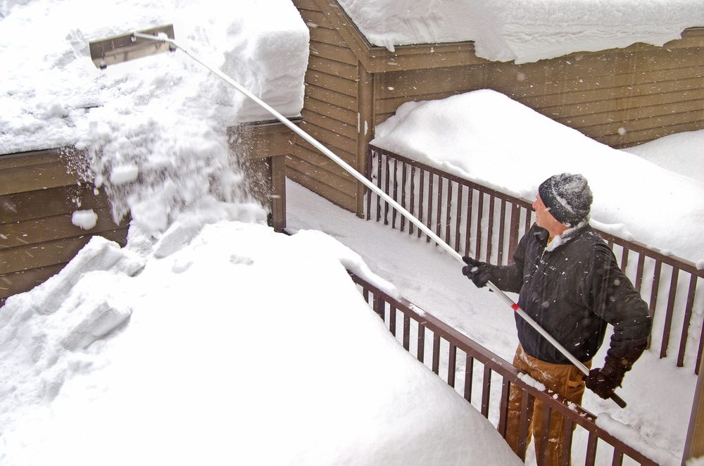 A man using a snow rake to remove snow from the roof in winter