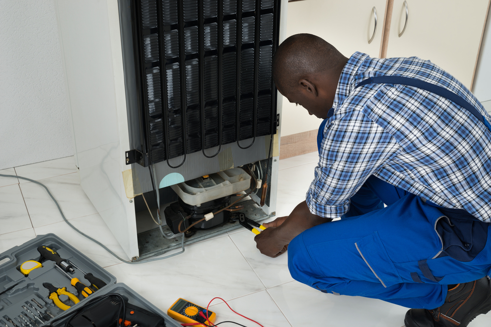 Young African American man fixing a refrigerator