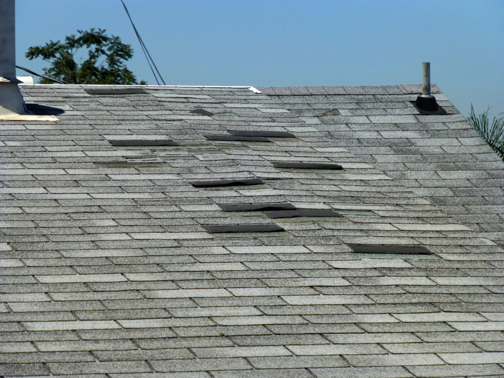 Shingles peeling off a worn, grey roof