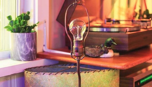 a lamp with the shade off in the corner of a living room with a record player behind it