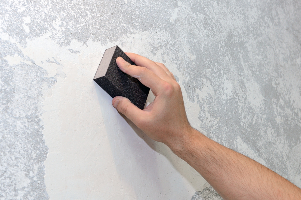 A hand sanding the wall