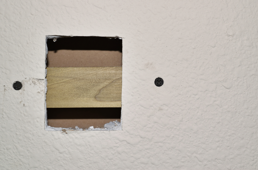 A damaged drywall square with a screwed-in wooden brace