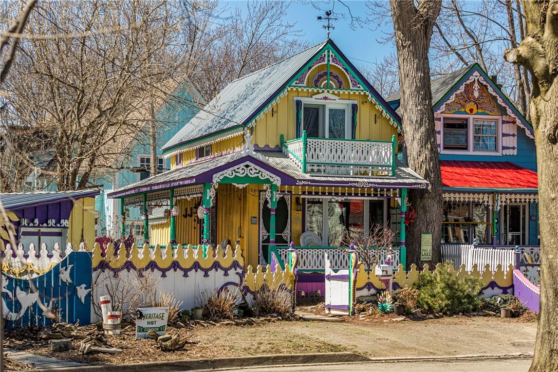 Colourful cottage with yellow exterior and purple, turquoise, and white trim. Gingerbread-style woodcarvings throughout.