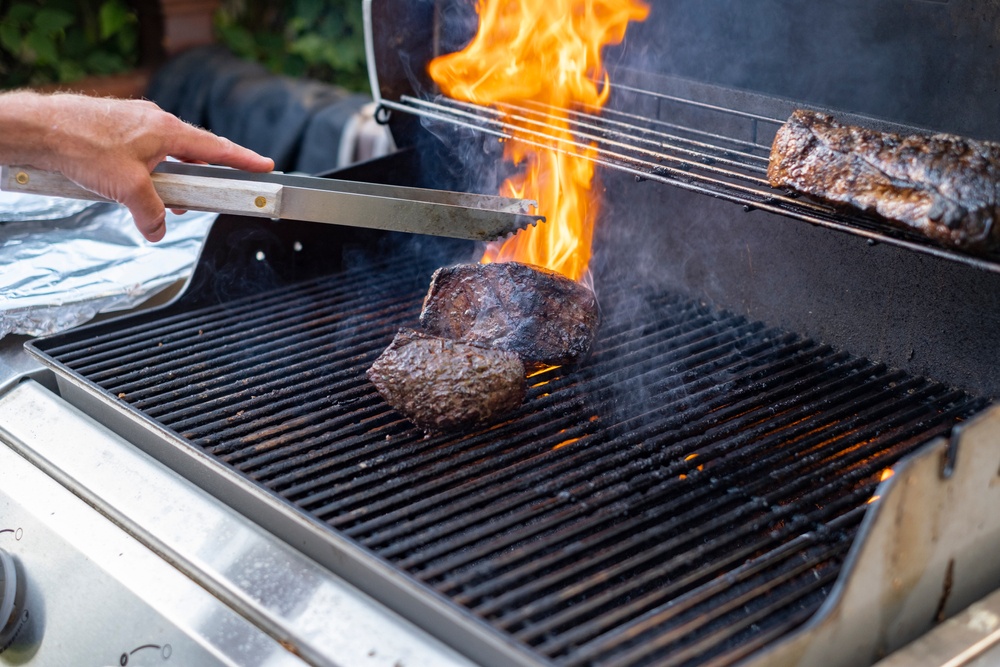 A man grilling beef on the barbecue as it flares up