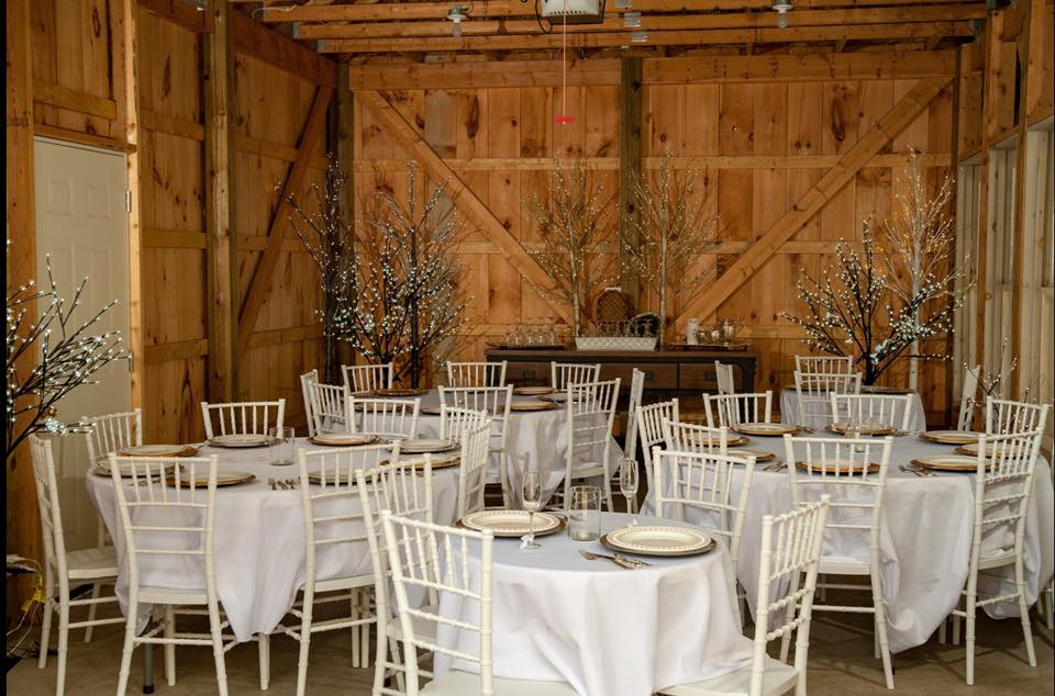 White chairs and tables draped in white linen inside a small wooden barn.