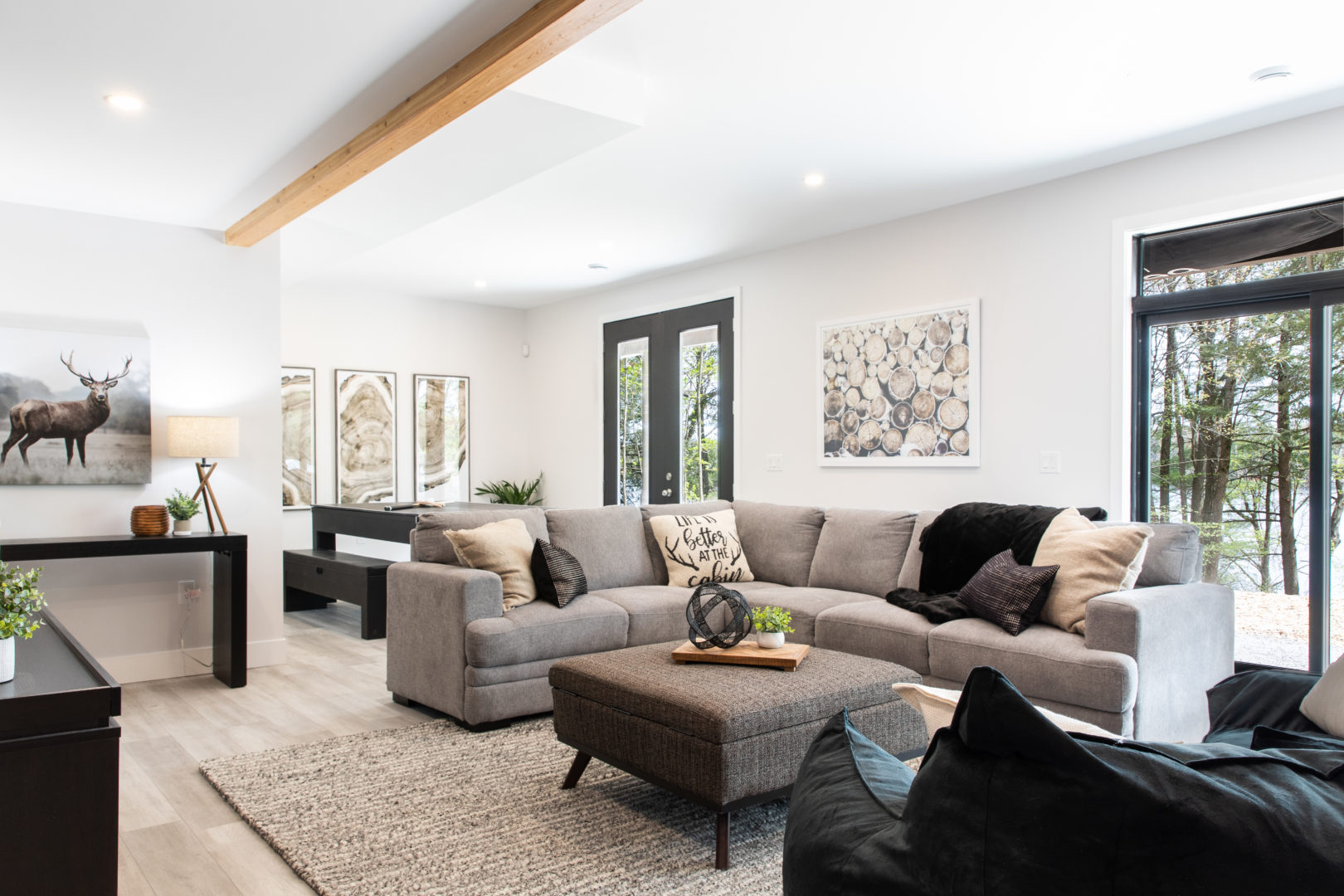 A bright basement living room with a big grey couch and a gam table behind it.