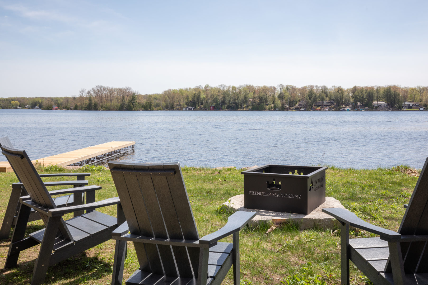 A spacious lakefront area with a long private dock and adirondak chairs gathered around a fire pit.