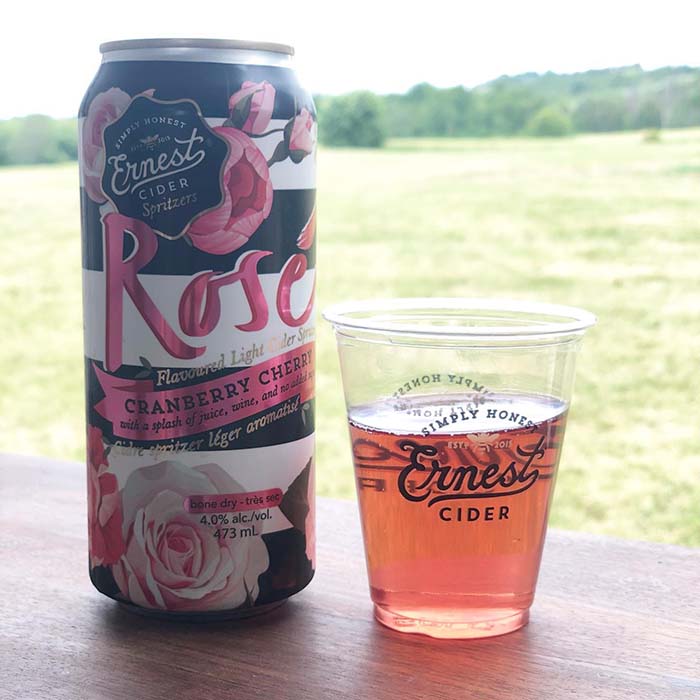 ernest cider rosé cranberry cherry light civer poured into a plastic cup in front of a field