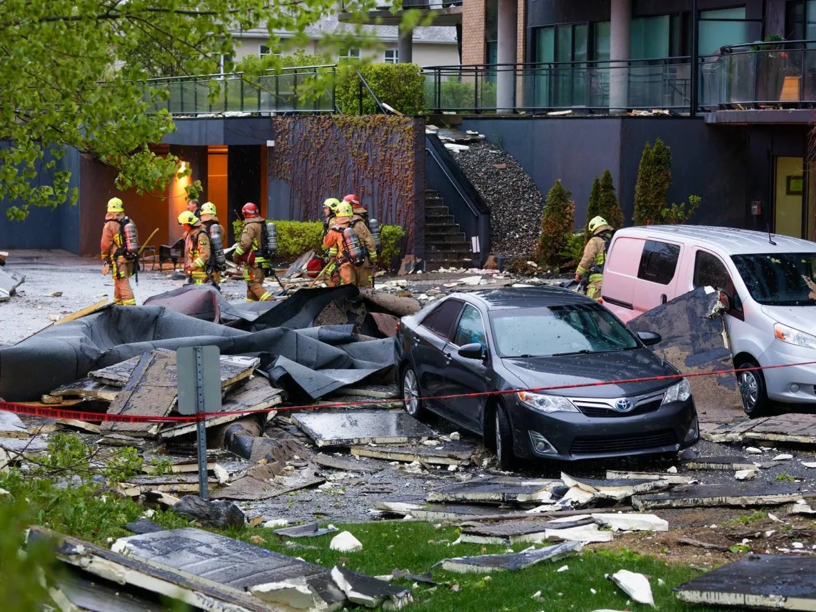 Emergency response workers at a scene with fallen debris in a parking lot with cars near a residential building.