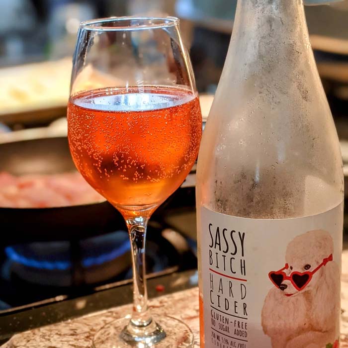 close-up of Hounds of Erie Winery's Sassy Bitch Cider in a wine glass next to the bottle