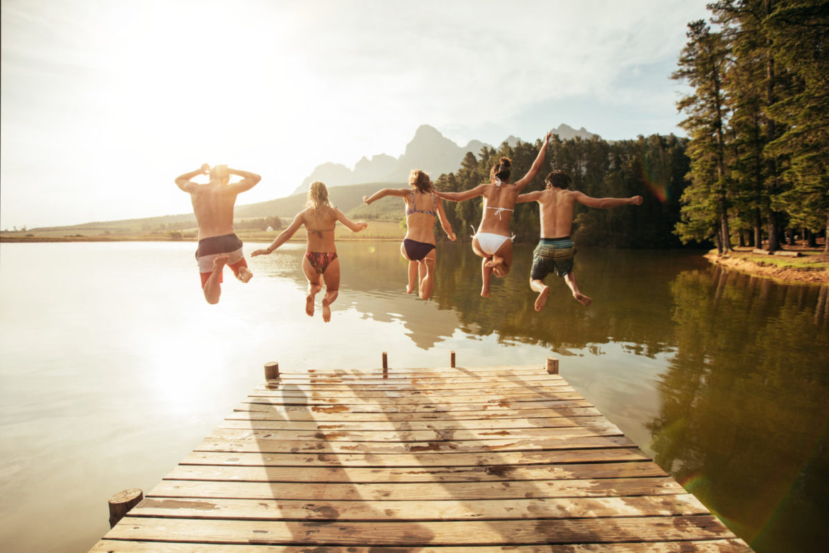 Friends jumping off a dock into a lake in the summer.