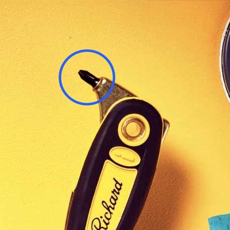 The end of a handle on a painter's combination tool with a small screw driver top.