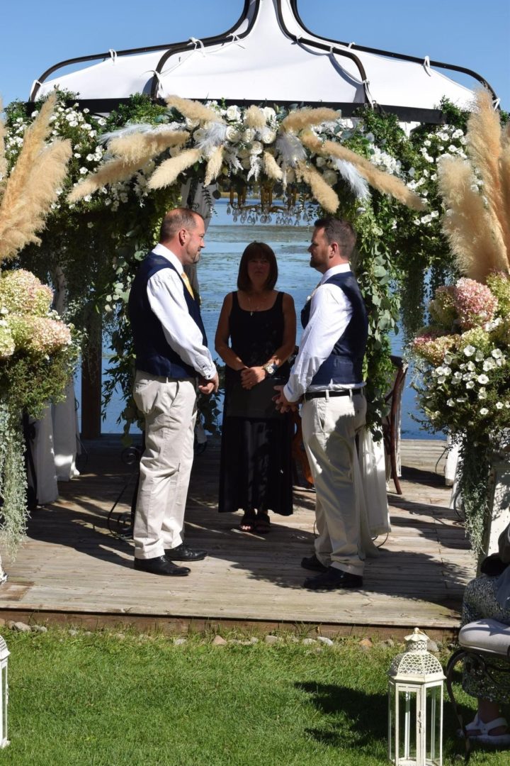 A couple getting married under a floral alter, in front of a blue lake.