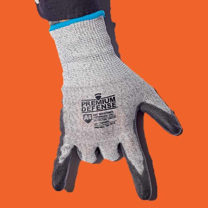 A hand wearing grey Premium Defense cut resistant gloves against an orange background.