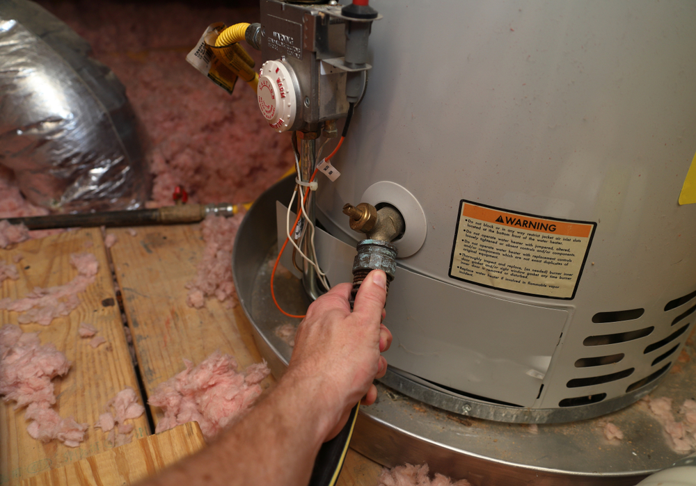 A hand attaching a hose to a home hot water heater