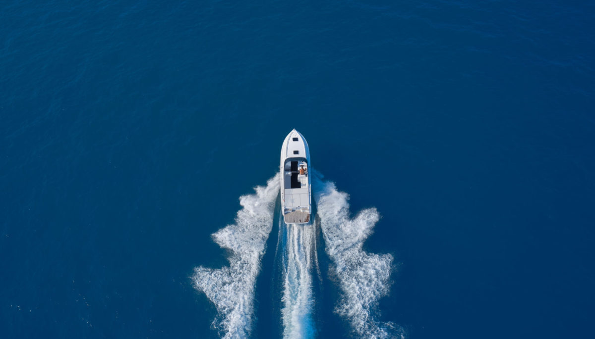 Bird's eye view of white speedboat driving along the blue lake water, creating waves.