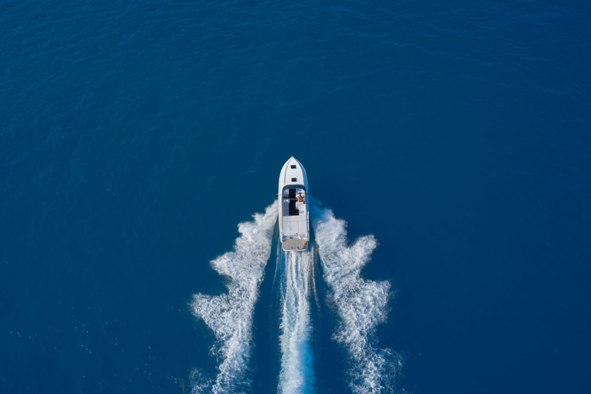 Bird's eye view of white speedboat driving along the blue lake water, creating waves.