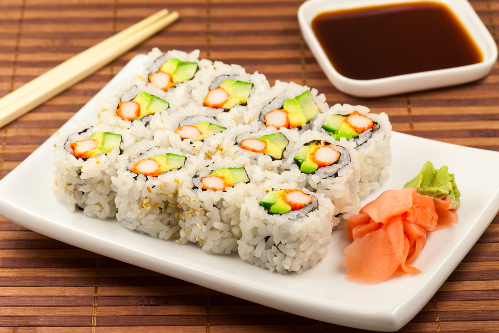 California rolls arranged on a white rectangular plate, with pickled ginger