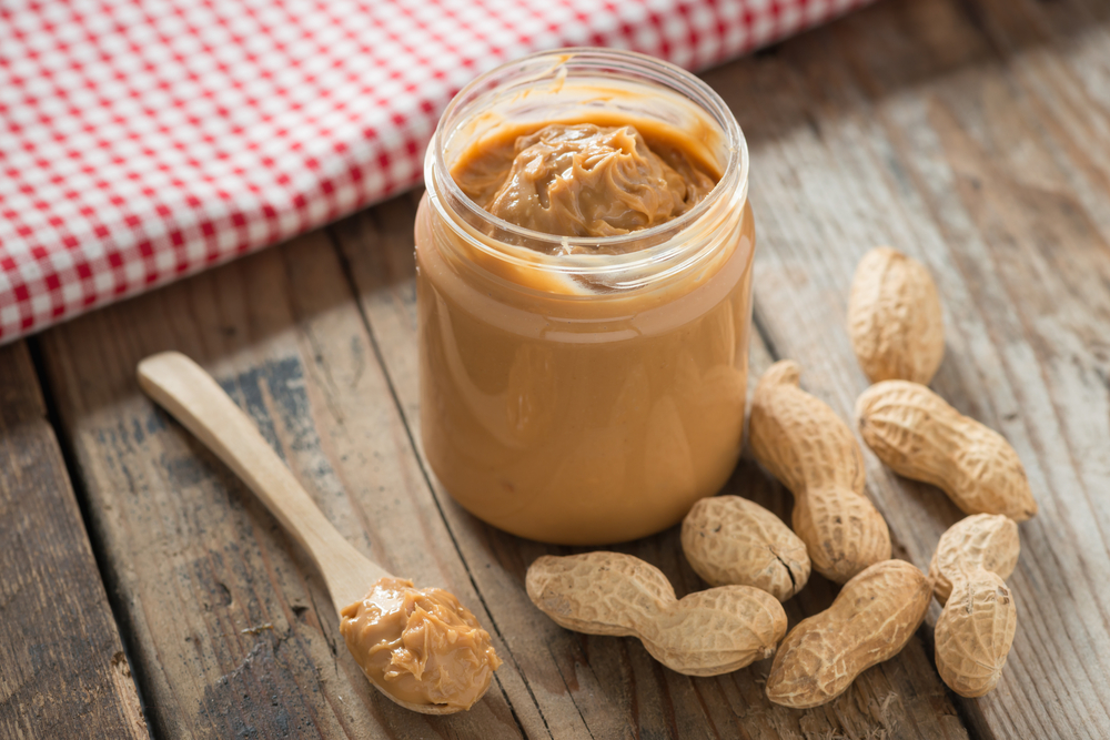 A jar of peanut butter on a table, surrounded by peanuts