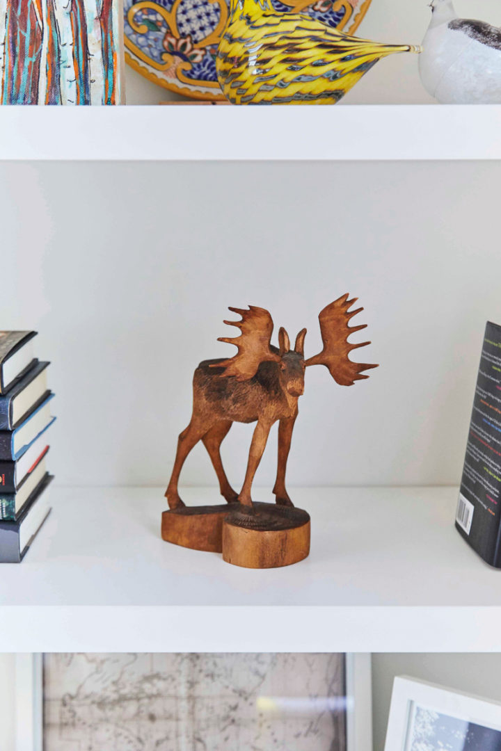 a small carved wooden moose sits on a bookshelf