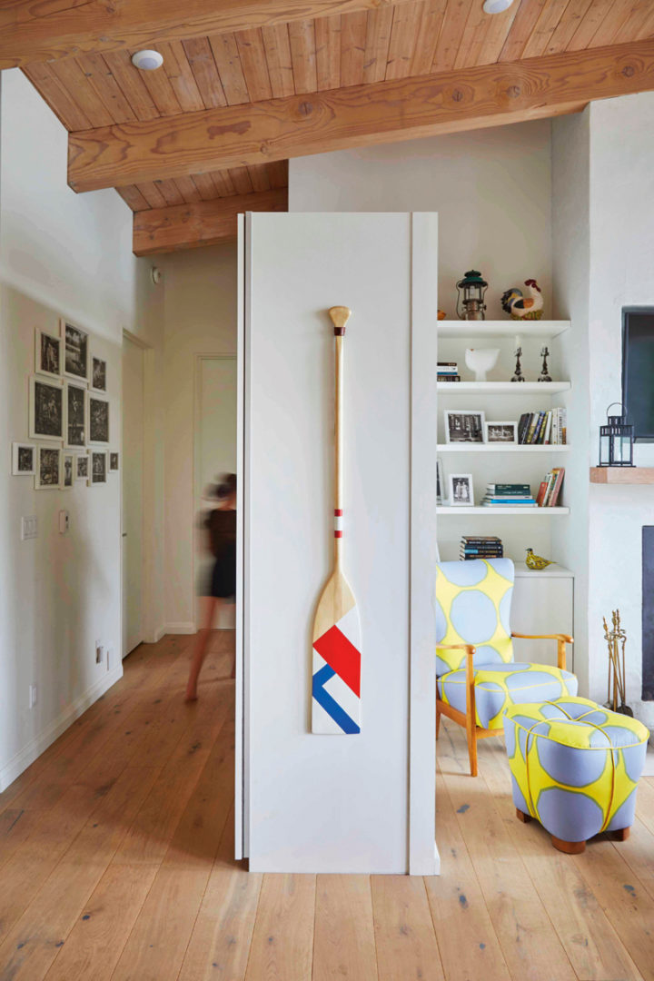 a marimekko fabric printed chair is in the livning room surrounded by white bookshelves. A painted paddle hangs on the end