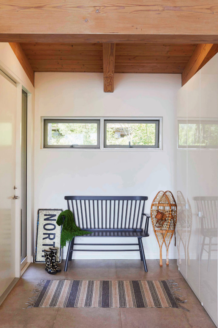 The entranceway of the Kelar's cottage with clerestory windows, a black bench, a pair of snowshoes, and a sign that says "North"