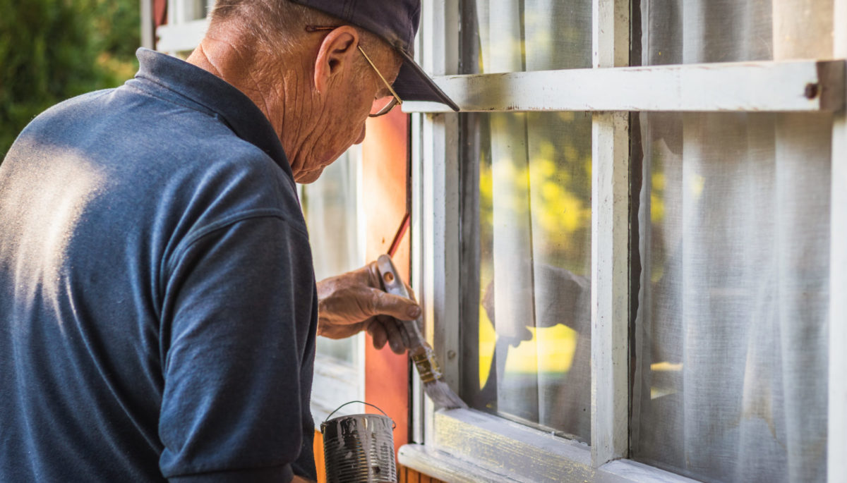 Man repairing window frame on a maturing cottage.