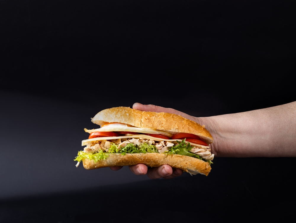 A hand holding a hoagie sandwich against a dark background