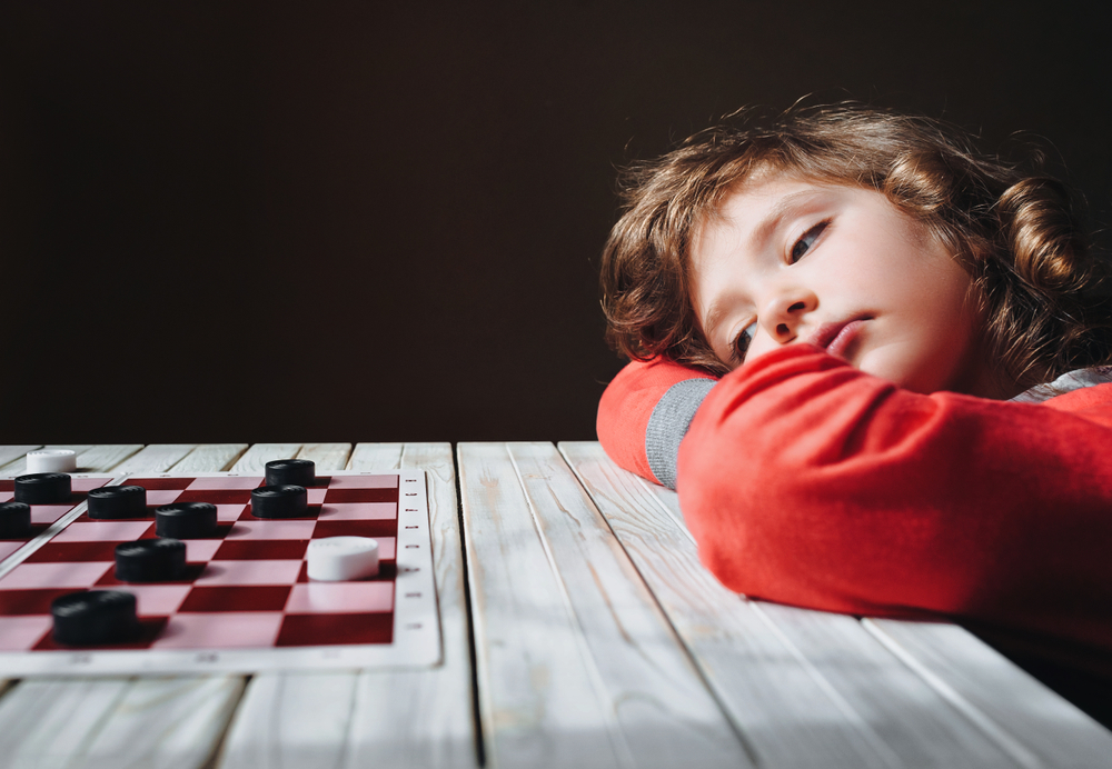 A bored child in front of a checker game