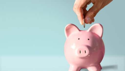 a hand putting a coin in a piggy bank on a blue background, budget