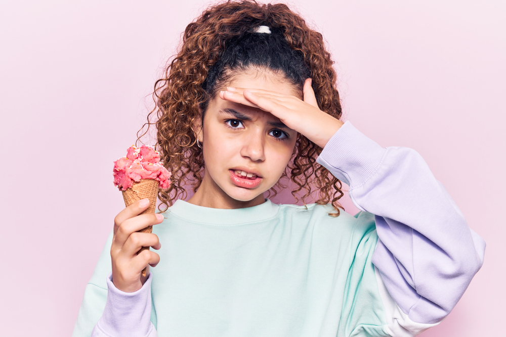 A girl holding an ice cream cone in one hand and her head in the other hand