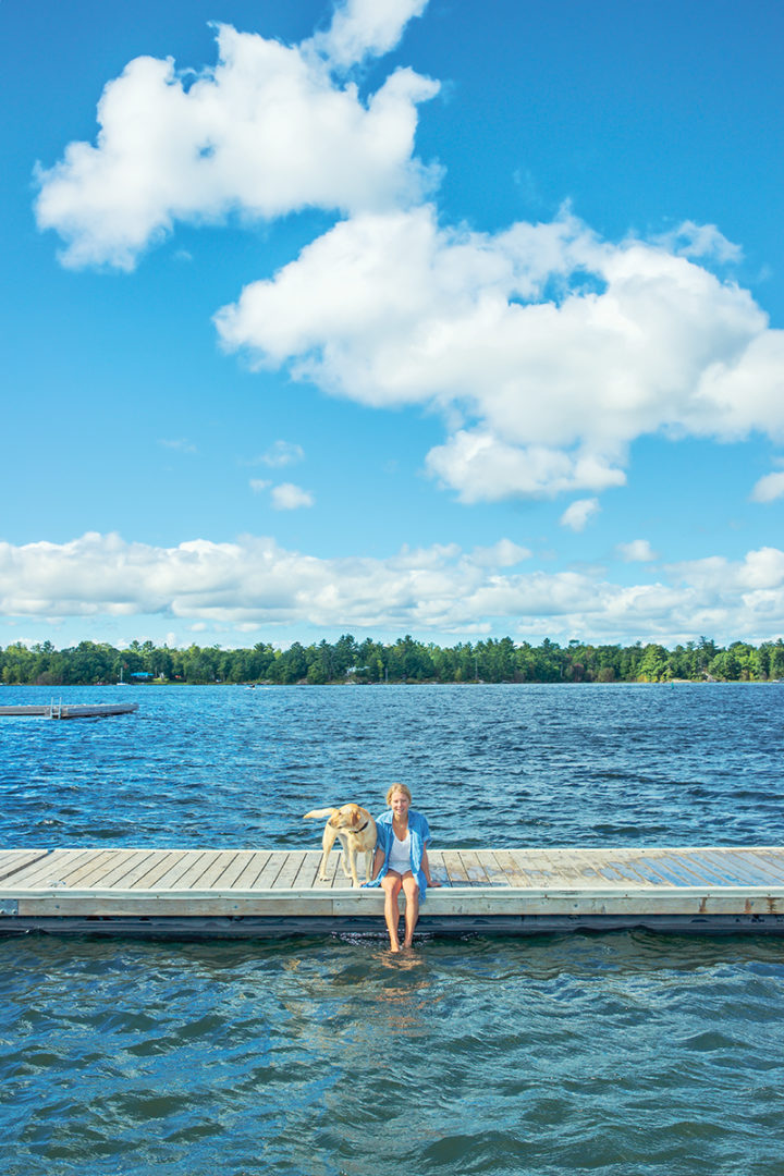 a young cottager sits on her dock on a lake beside her golden lab