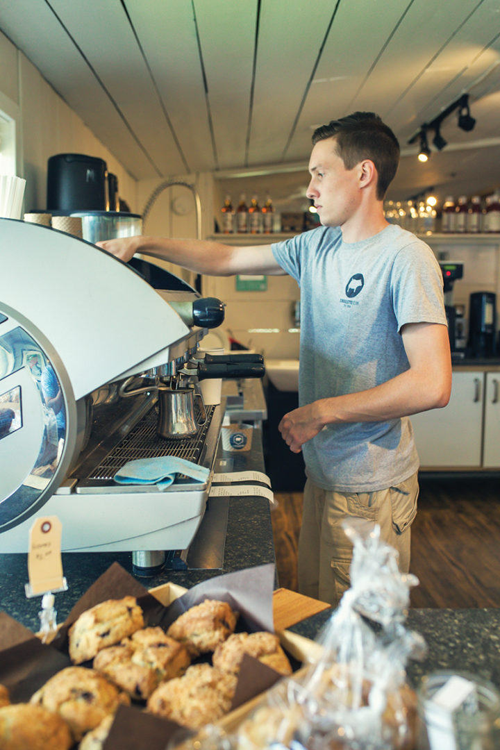 a man operates a coffee machine inside The Hive store next to stop baked goods