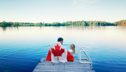 A father and daughter sitting on the dock, wrapped in a Canadian flag