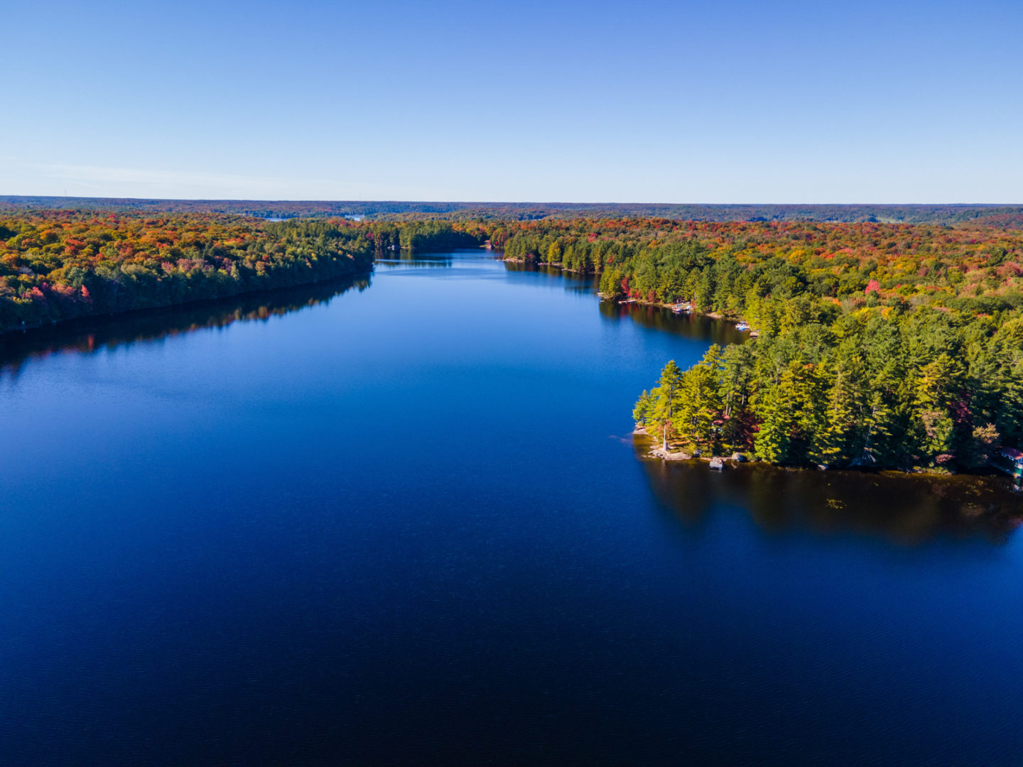 Overhead shot of a deep blue lake with green and orange trees on the shore.