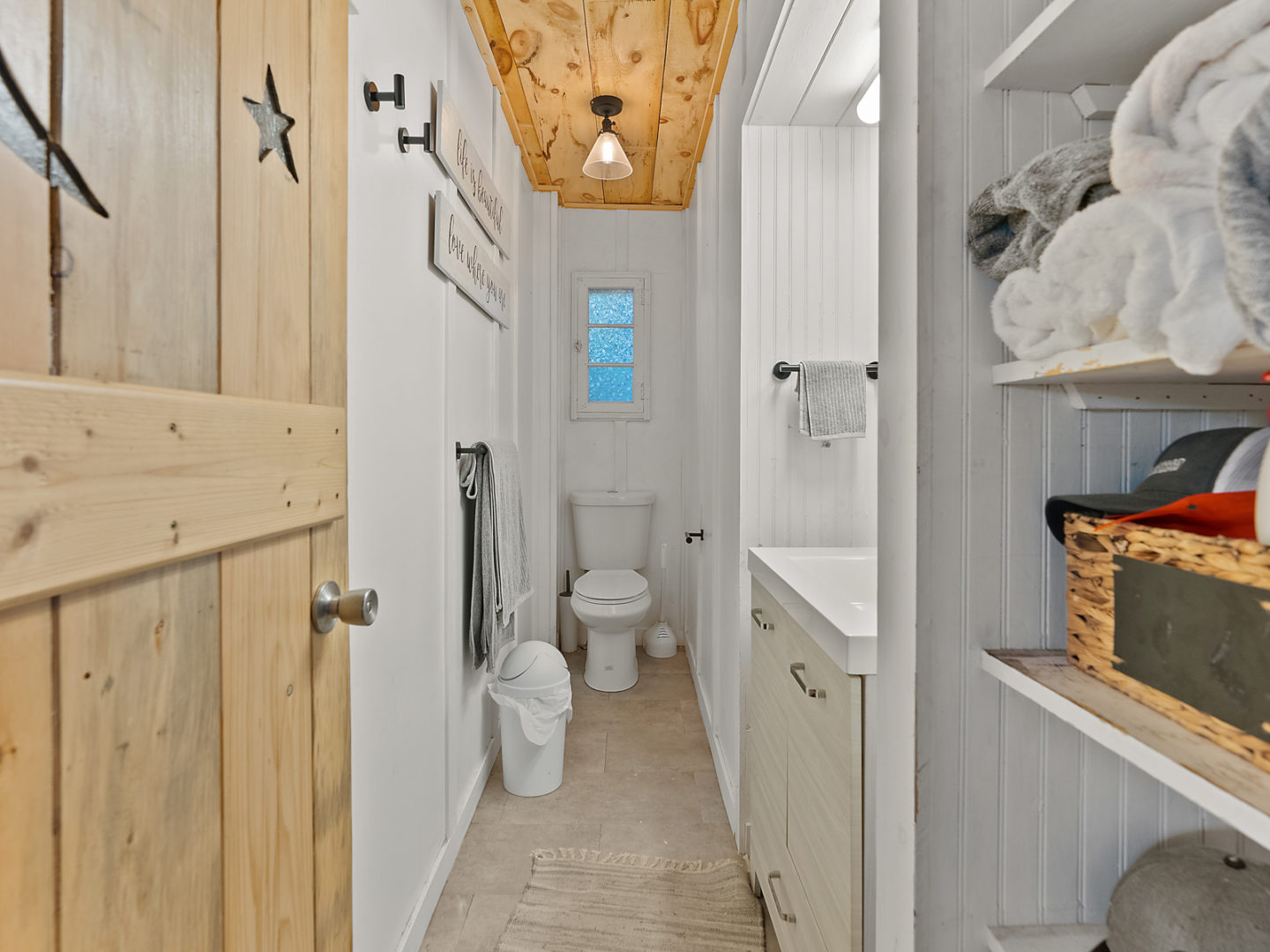 A small bathroom with a toilet, sink, and shelving space.
