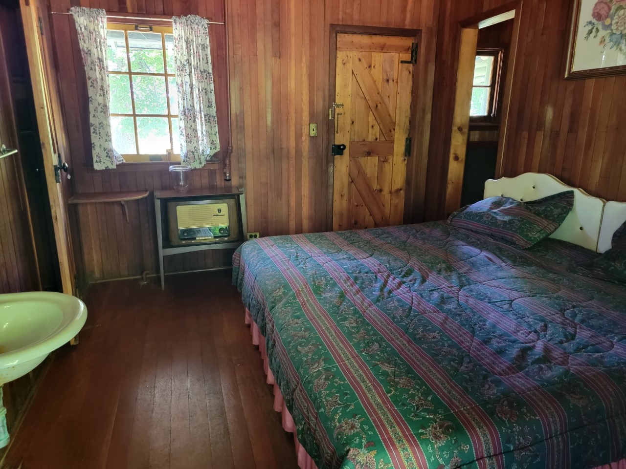 Interior bedroom with wood floors, a large bed and a sink in the room.